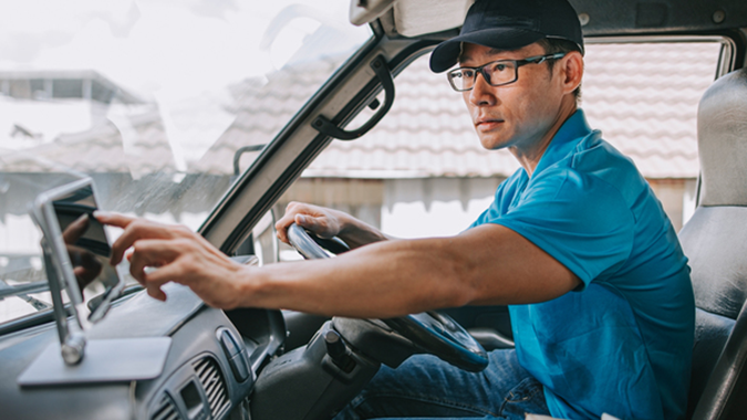 Delivery driver sitting in cab of truck using a tablet device