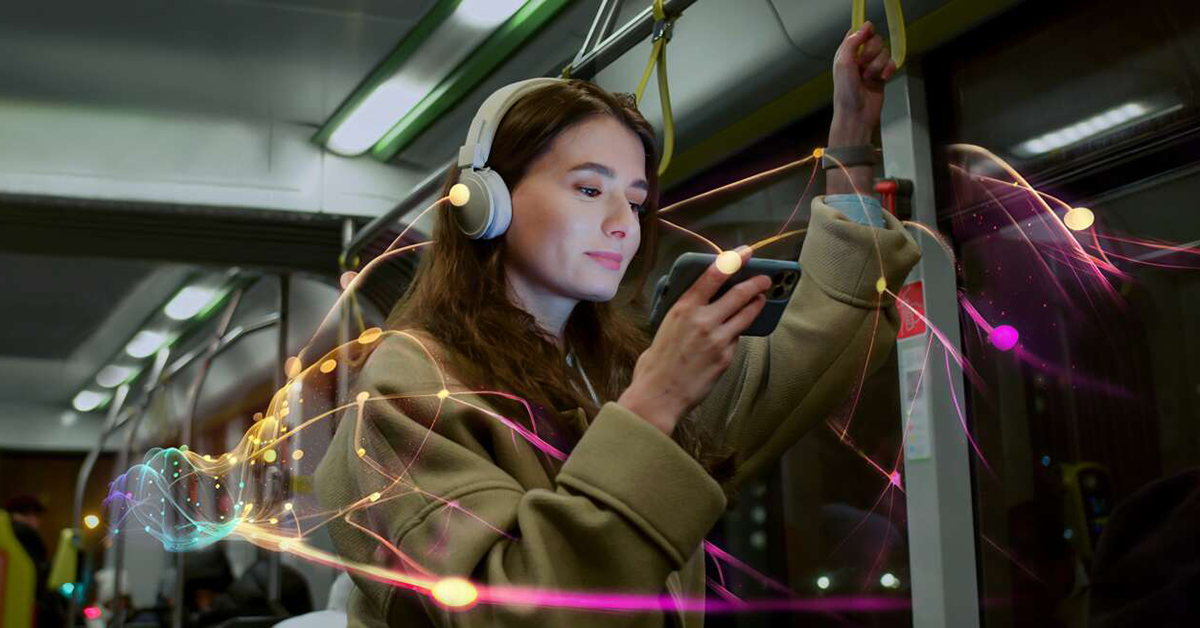 Woman wearing headphones and looking on her phone while riding in a bus.